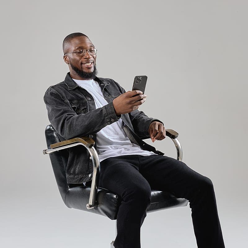 A smiling barber seated in a shop chair, looking at his phone
