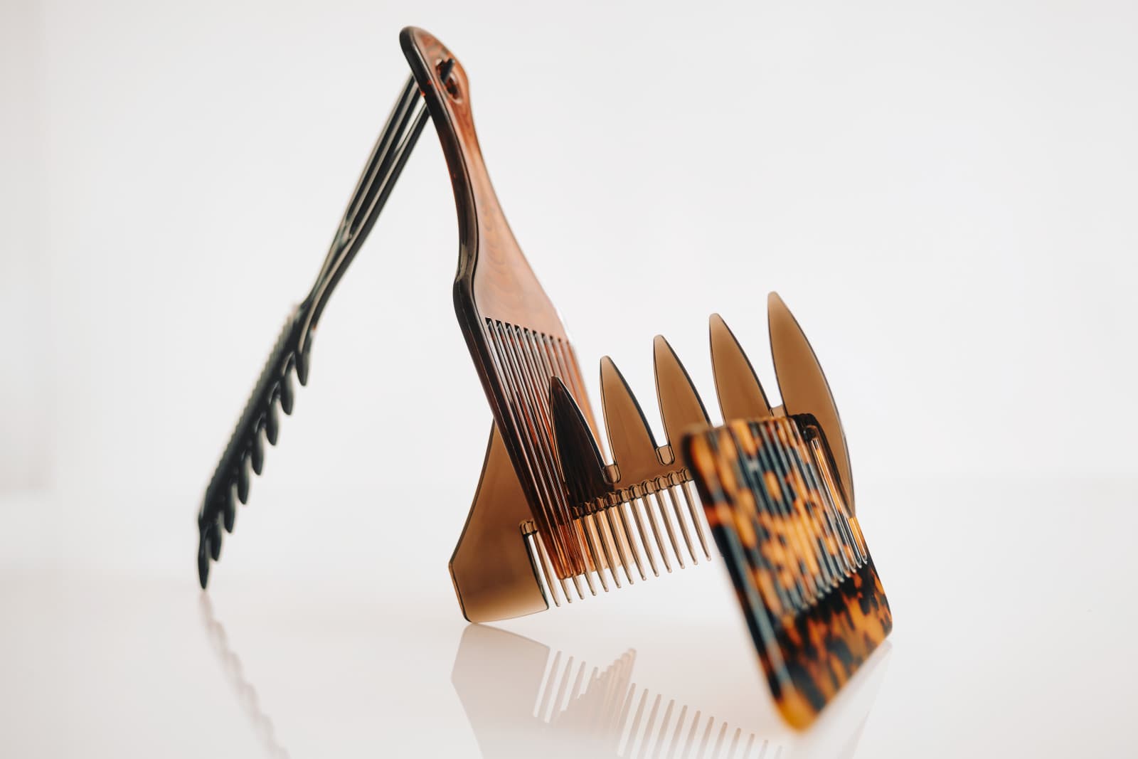 A trio of handcrafted Oak & Steel combs — tortoiseshell, amber, and black — standing on a bright, reflective countertop