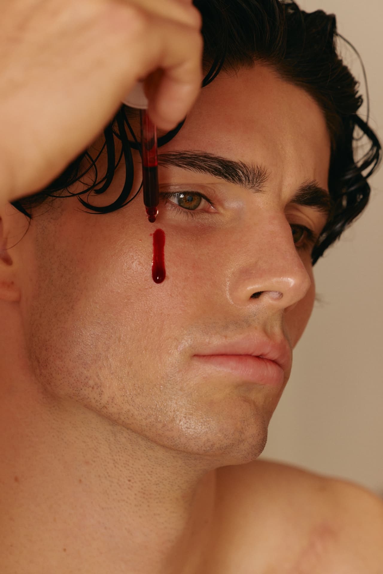 A close-up of a man’s face as a dropper releases a single red drop of serum beside his eye