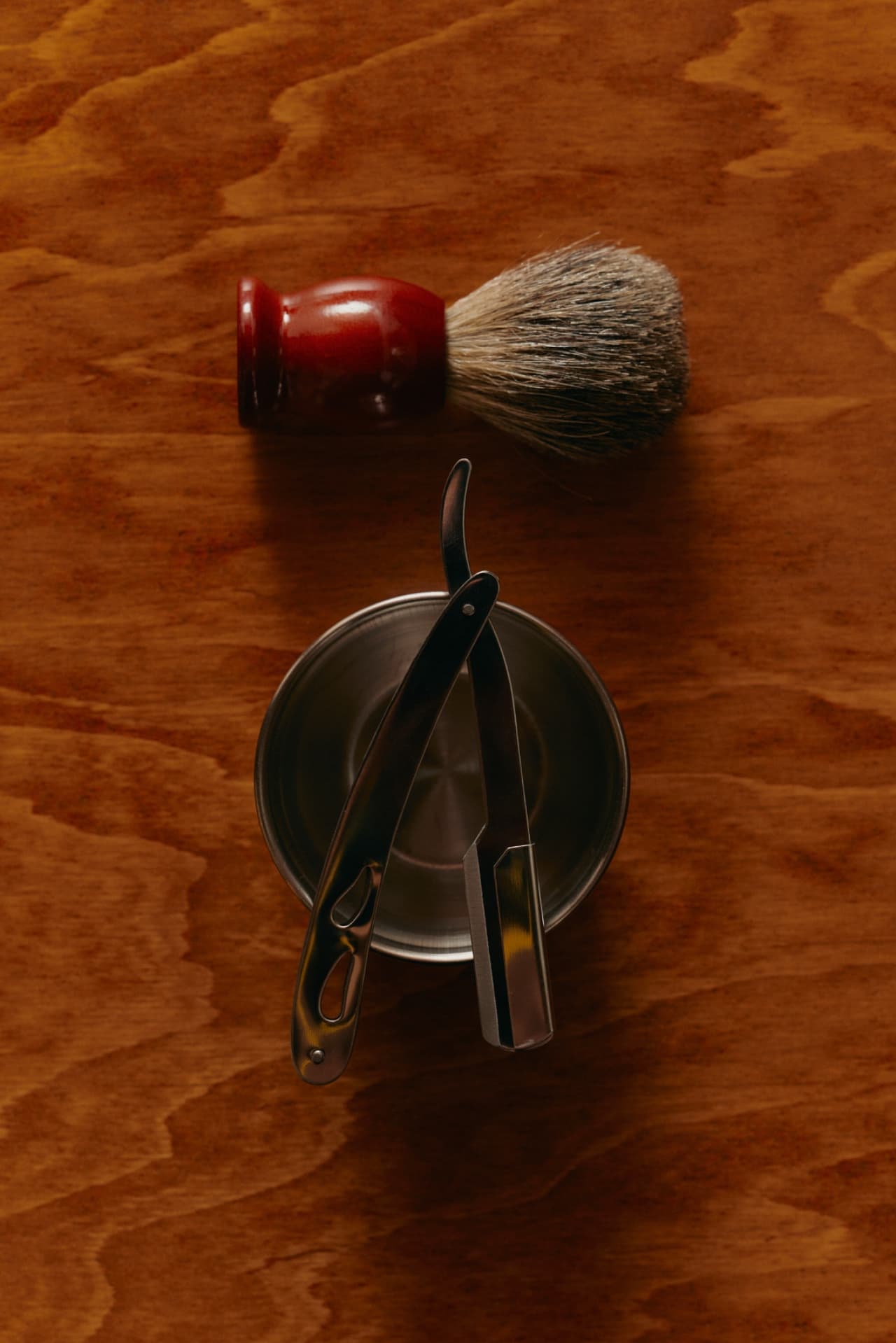 A straight razor and badger-hair shaving brush resting on a metal shaving bowl at Oak & Steel