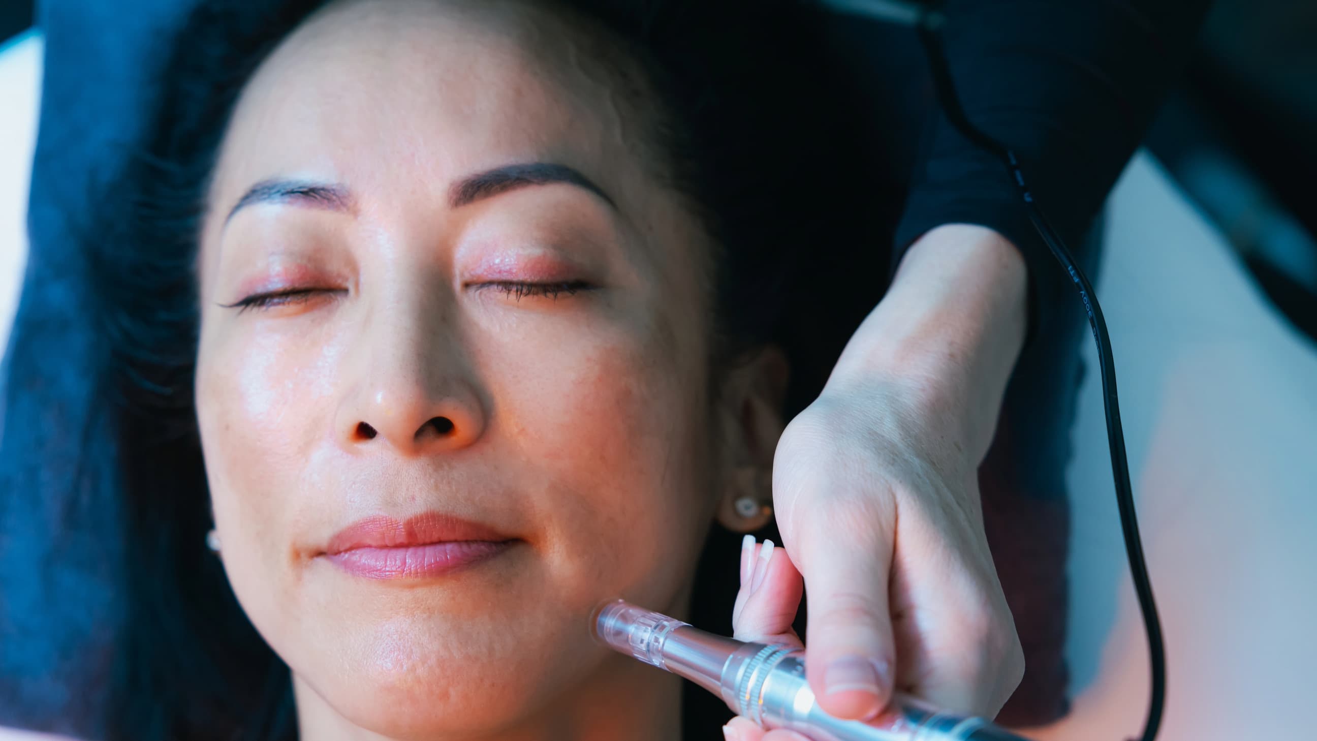 A woman lies on a table with her eyes closed as she receives a skin care treatment.