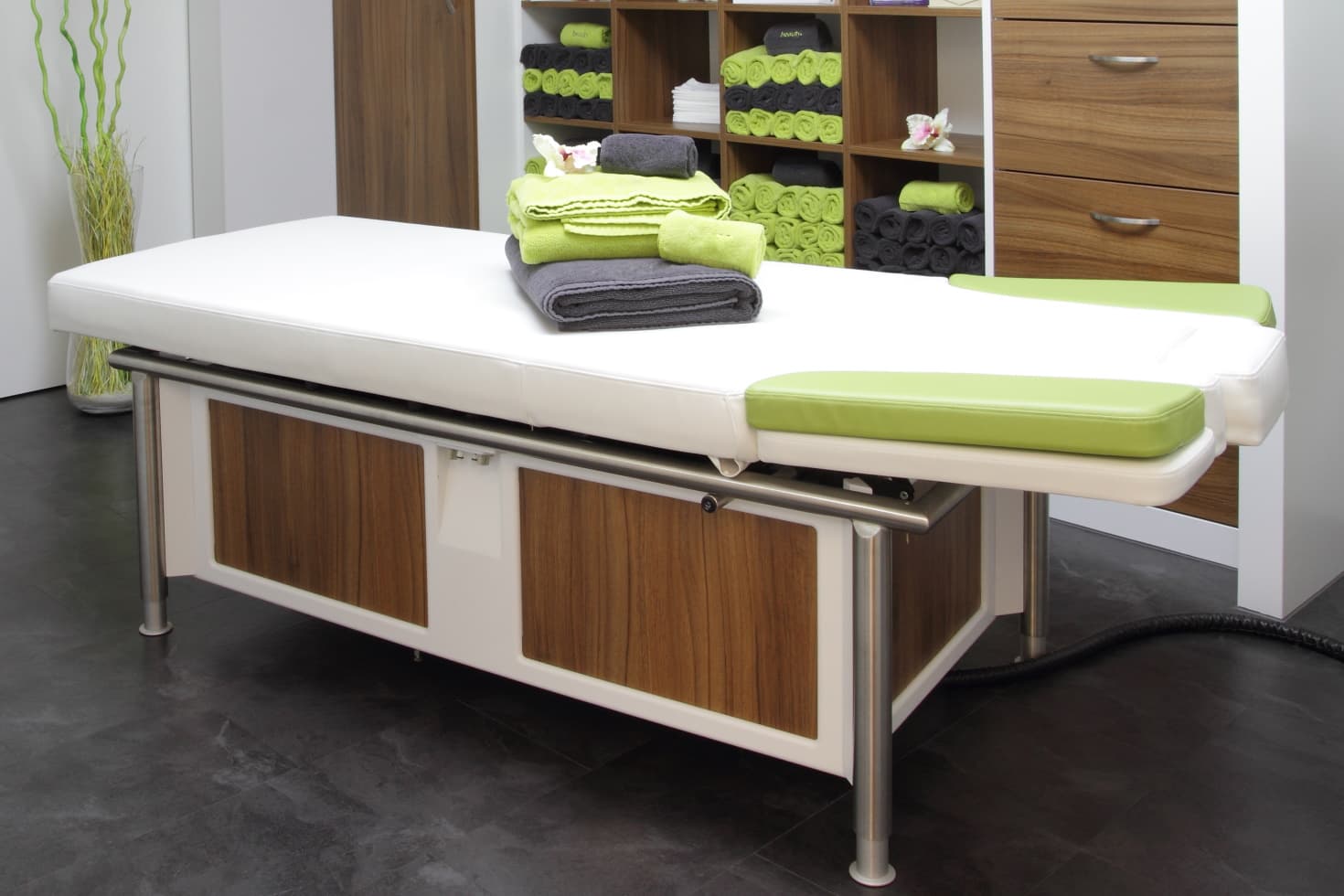 An adjustable massage table with several different-colored towels neatly stacked on top