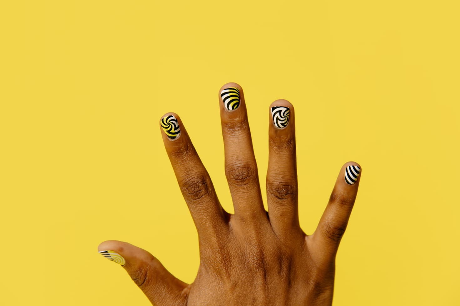 Showing off a manicure of swirling black and white lines against a bright yellow background