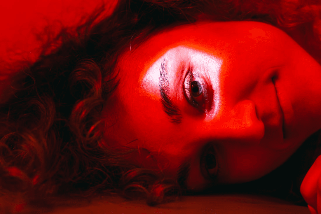 Close up of a woman's face in dim red light. There's a bright white spotlight on the eyebrow.