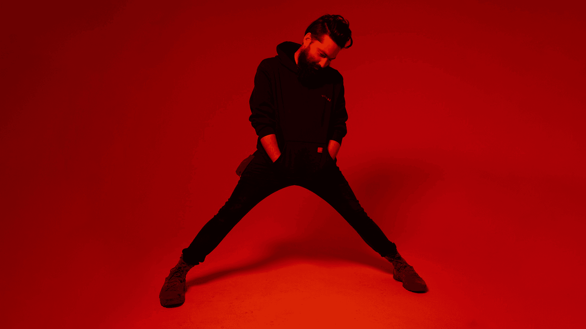 Boulevard Senior Art Director Wood Simmons, lit all in red on a blank studio background, stands in a broad stance with hands stuffed into his hoody pocket.