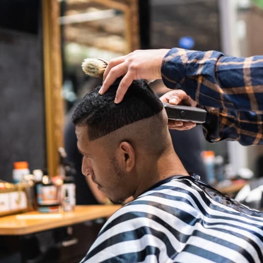 A barber uses an electric razor to cut a fade for his client.