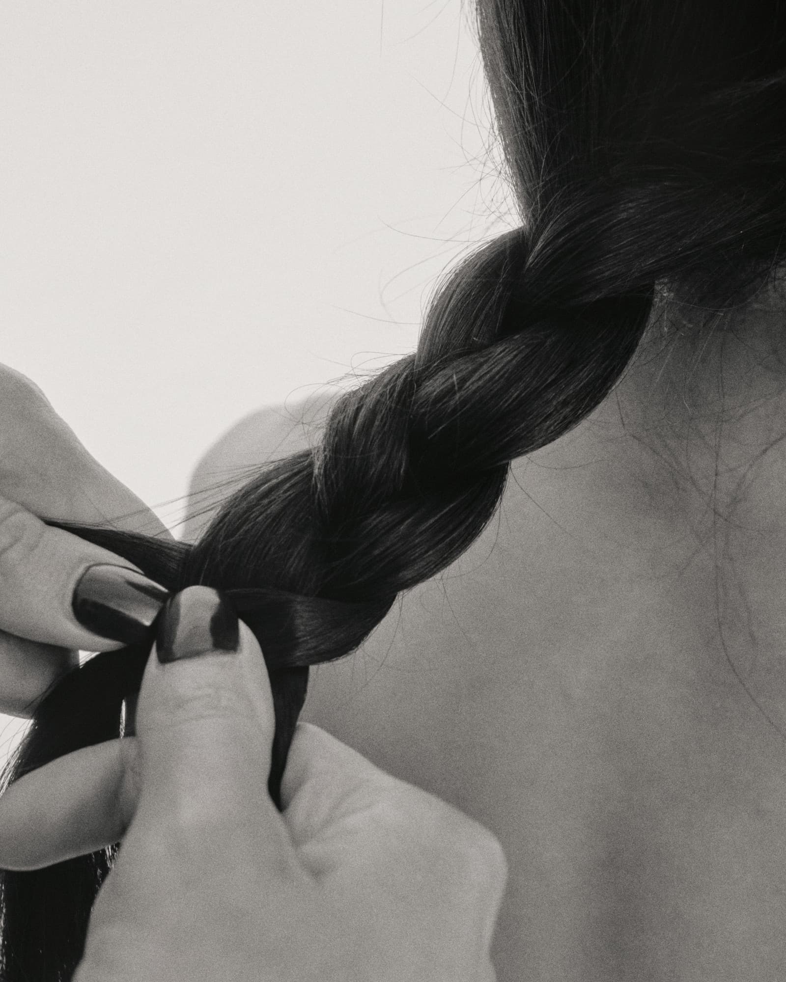 Hands finishing a loose braid in long dark hair, in black and white