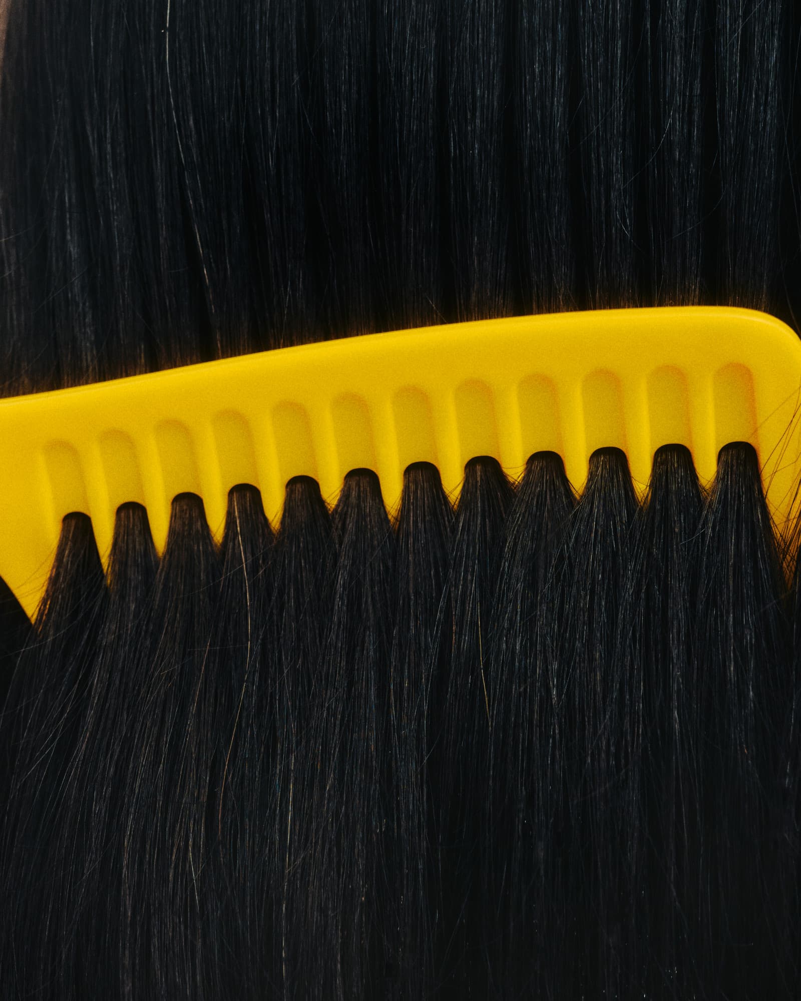 A yellow wide-tooth comb being pulled through long, straight black hair