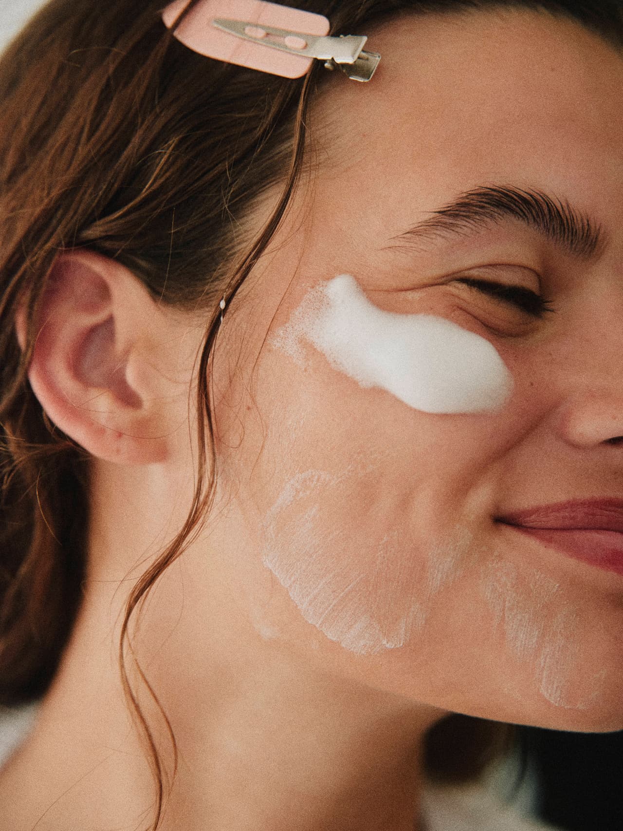 A smiling client with a clip holding back her hair while a skincare product is applied near her eye