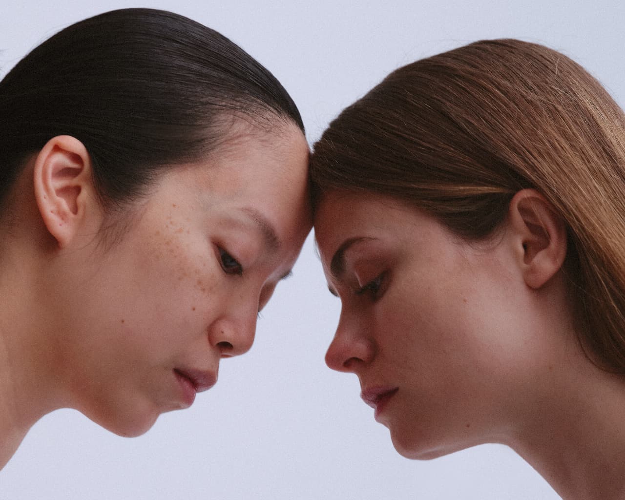 Two Face Foundrié clients rest forehead to forehead, showing clear, healthy skin