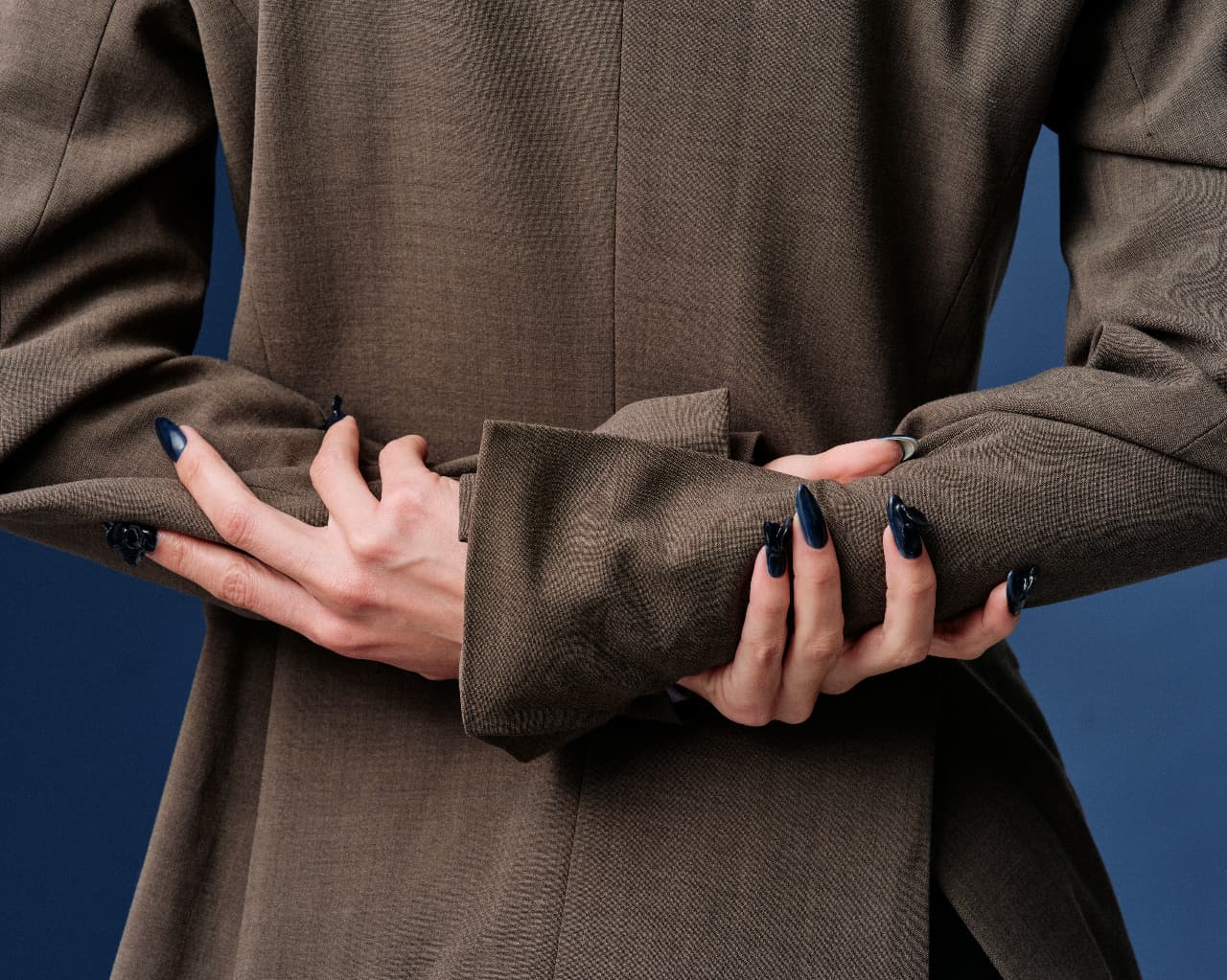 A close-up of clasped hands wearing glossy, dark manicured nails