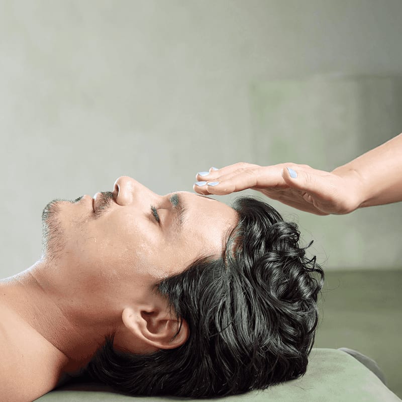 A spa therapist holding a hand over the forehead of a relaxed client lying on a treatment table