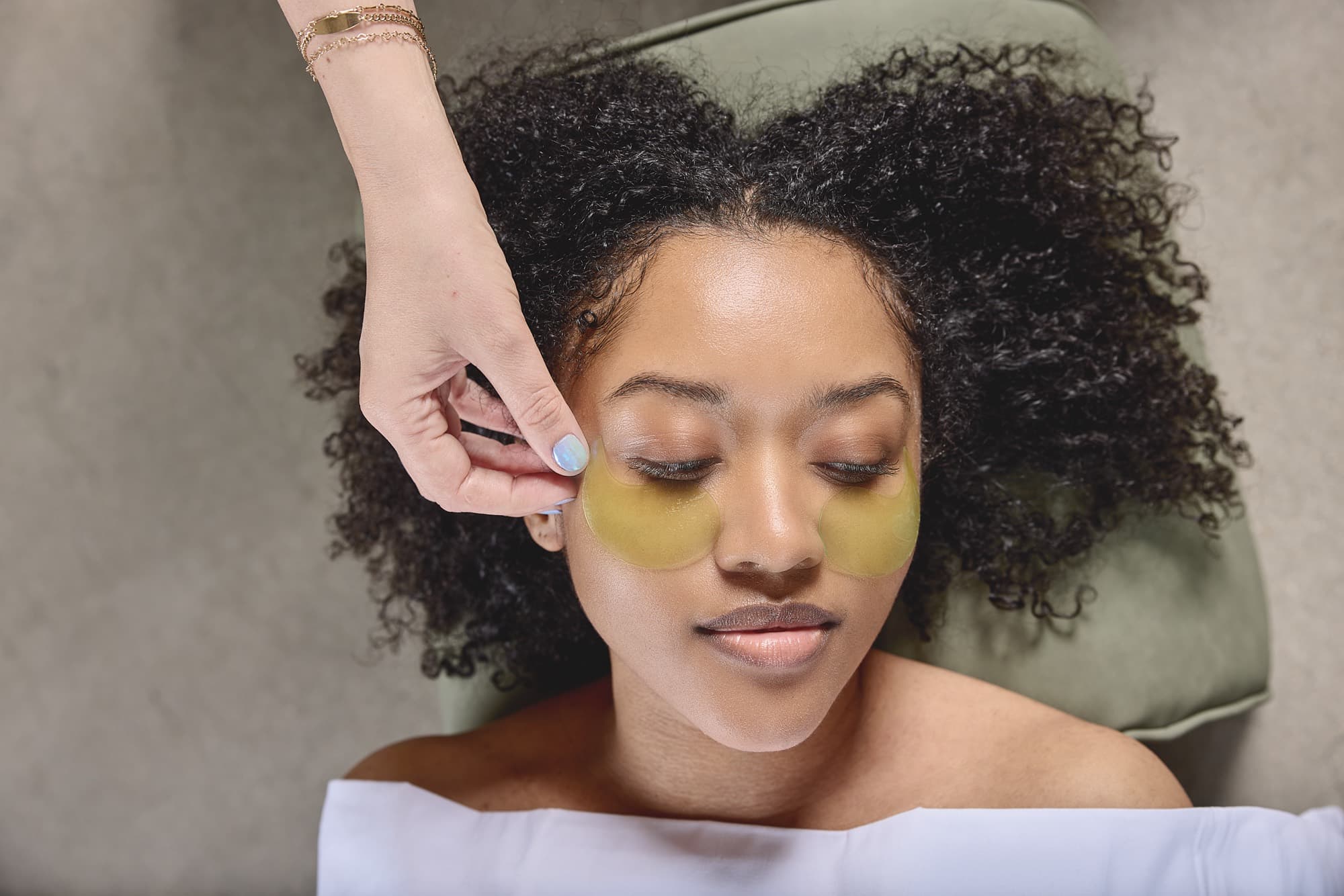 An aesthetician applying under-eye patches to a client