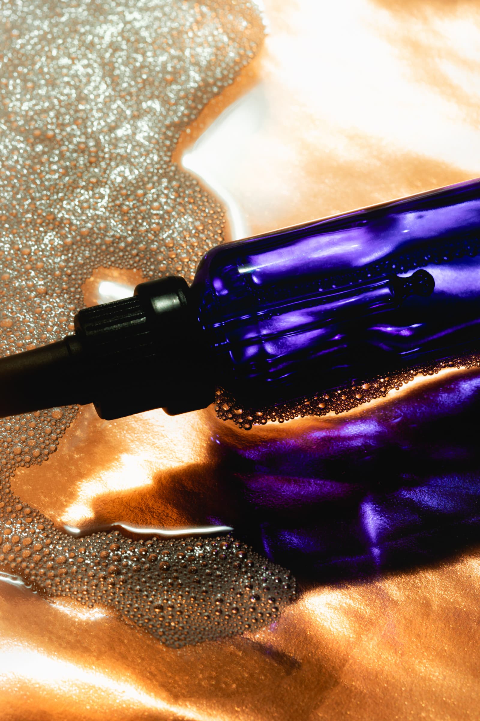 A cobalt-blue glass dropper bottle of Face Foundrié serum resting on a warm, foamy surface