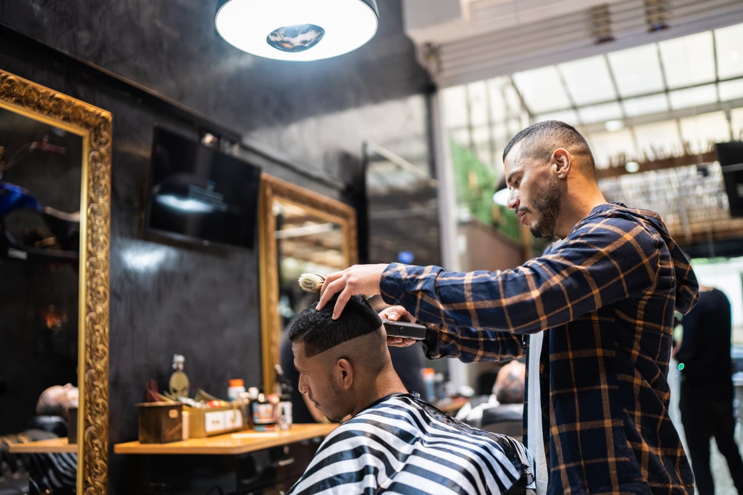 A barber uses an electric razor to cut a fade for his client.