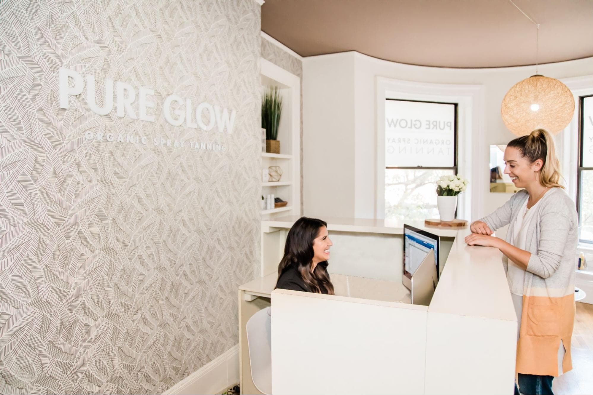 A spa receptionist smiles while checking in a client at the front desk, representing the personalized client relationships spa email marketing is built to support.