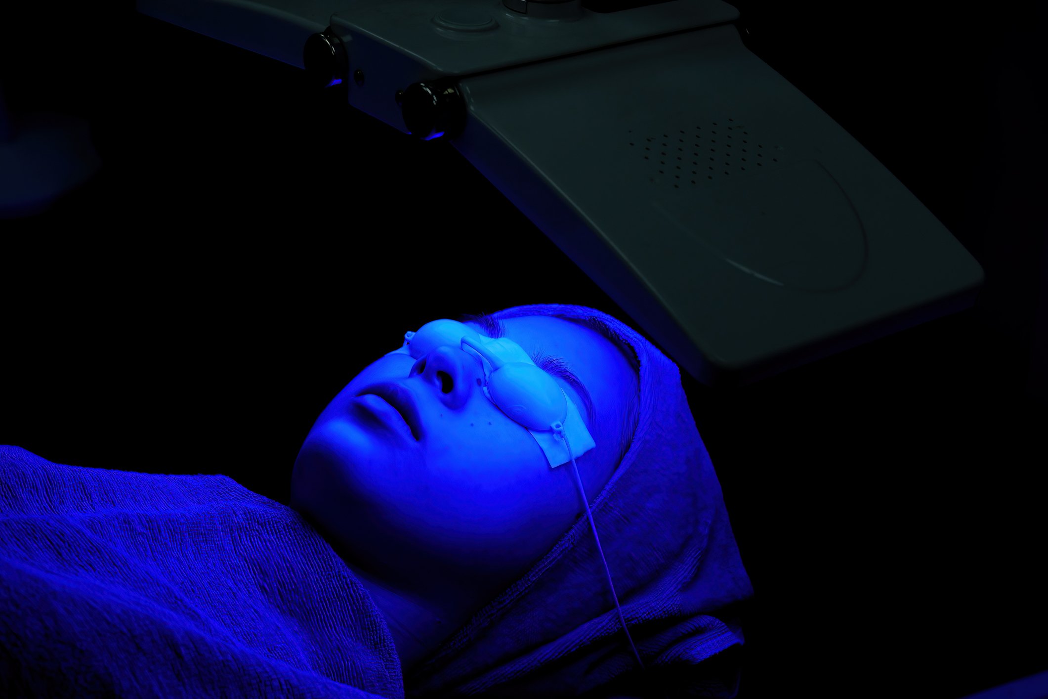 A medspa client receives blue light treatment in a dark room.