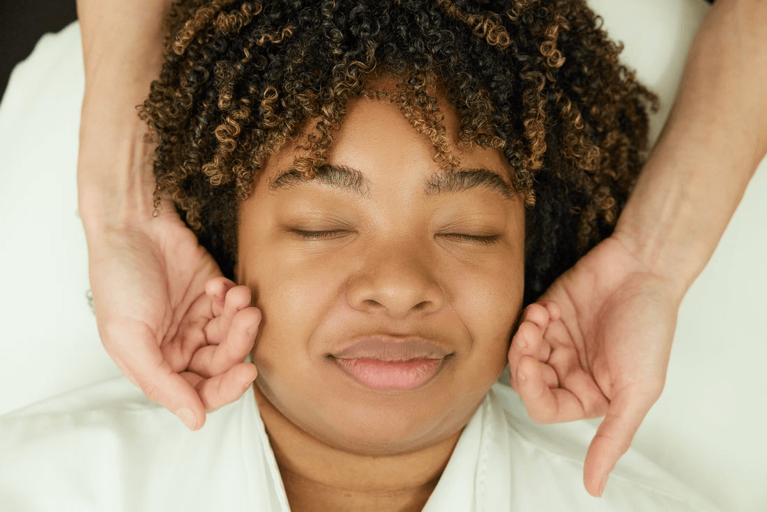 A person with their eyes closed receives a facial massage from a spa employee.