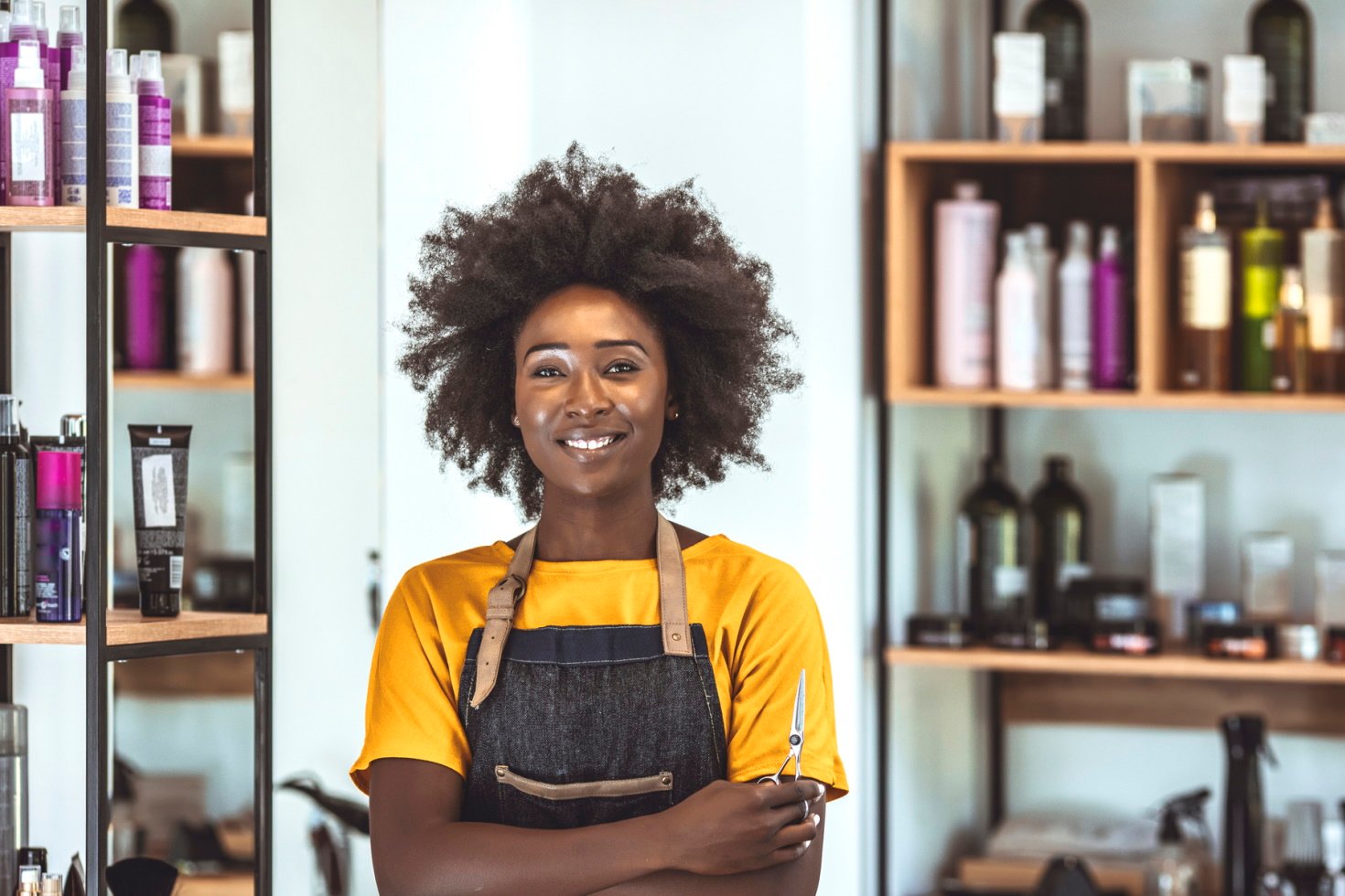 A young hair stylist stands in front of shelves stocked with hair care products.