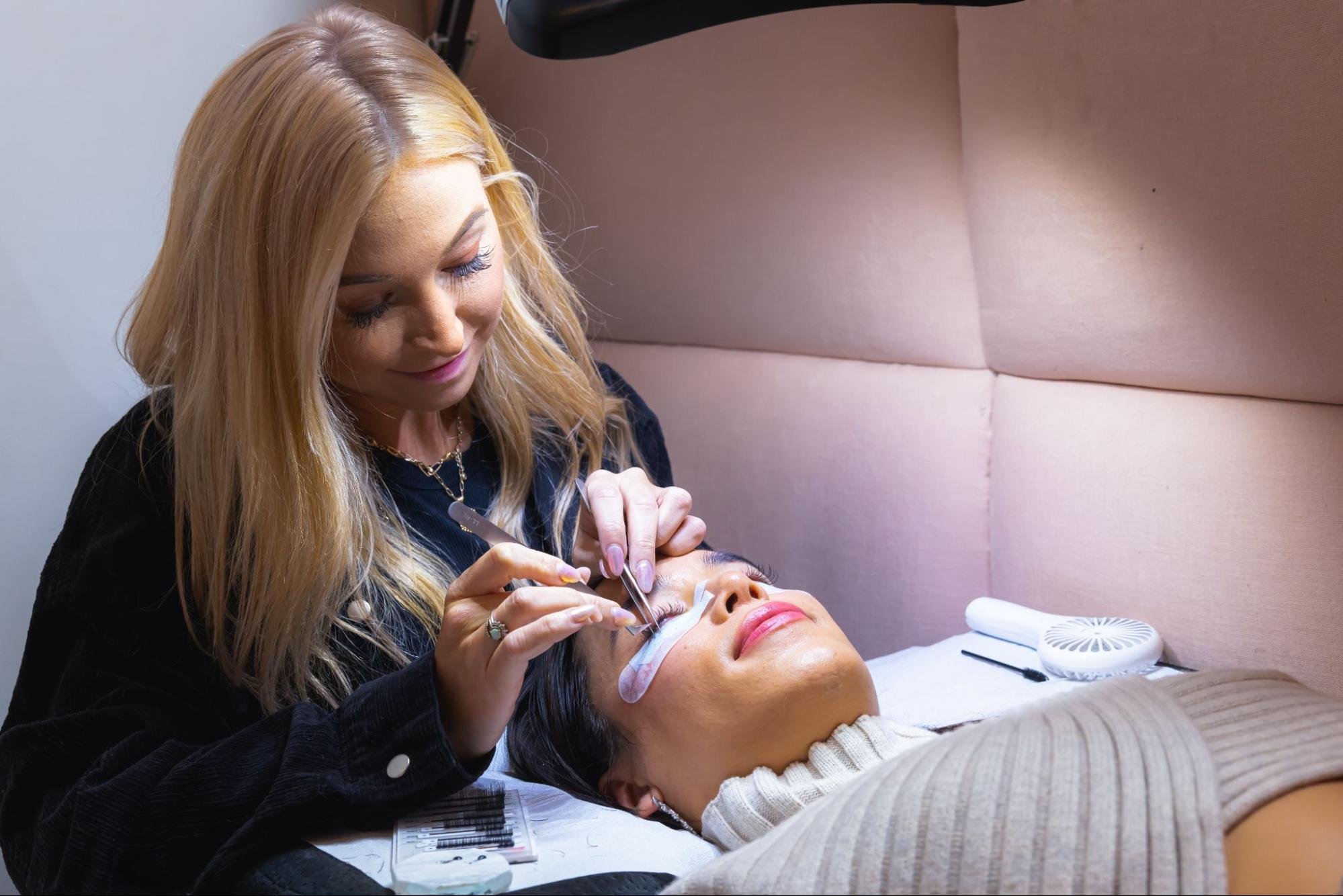An eyelash technician from BlinkBar performs a service for a satisfied client.