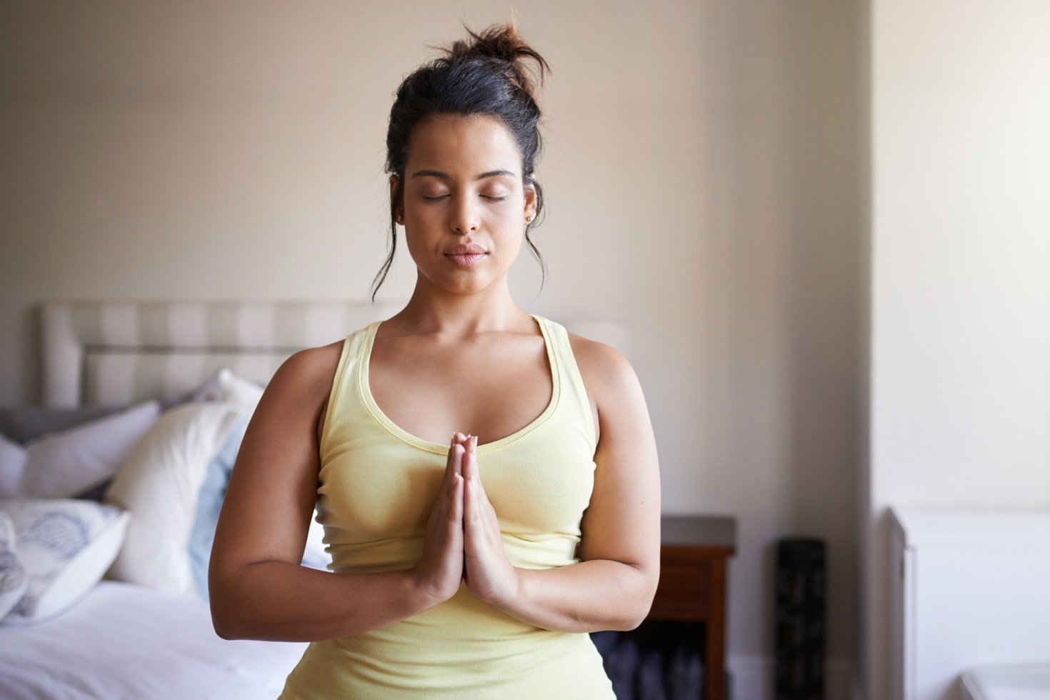 A young woman meditates with hands together in her bedroom