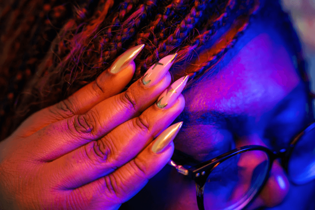 A close up of a woman's nails as she pushes up her glasses. The nail work is exquisite, in hues of gold and pink.