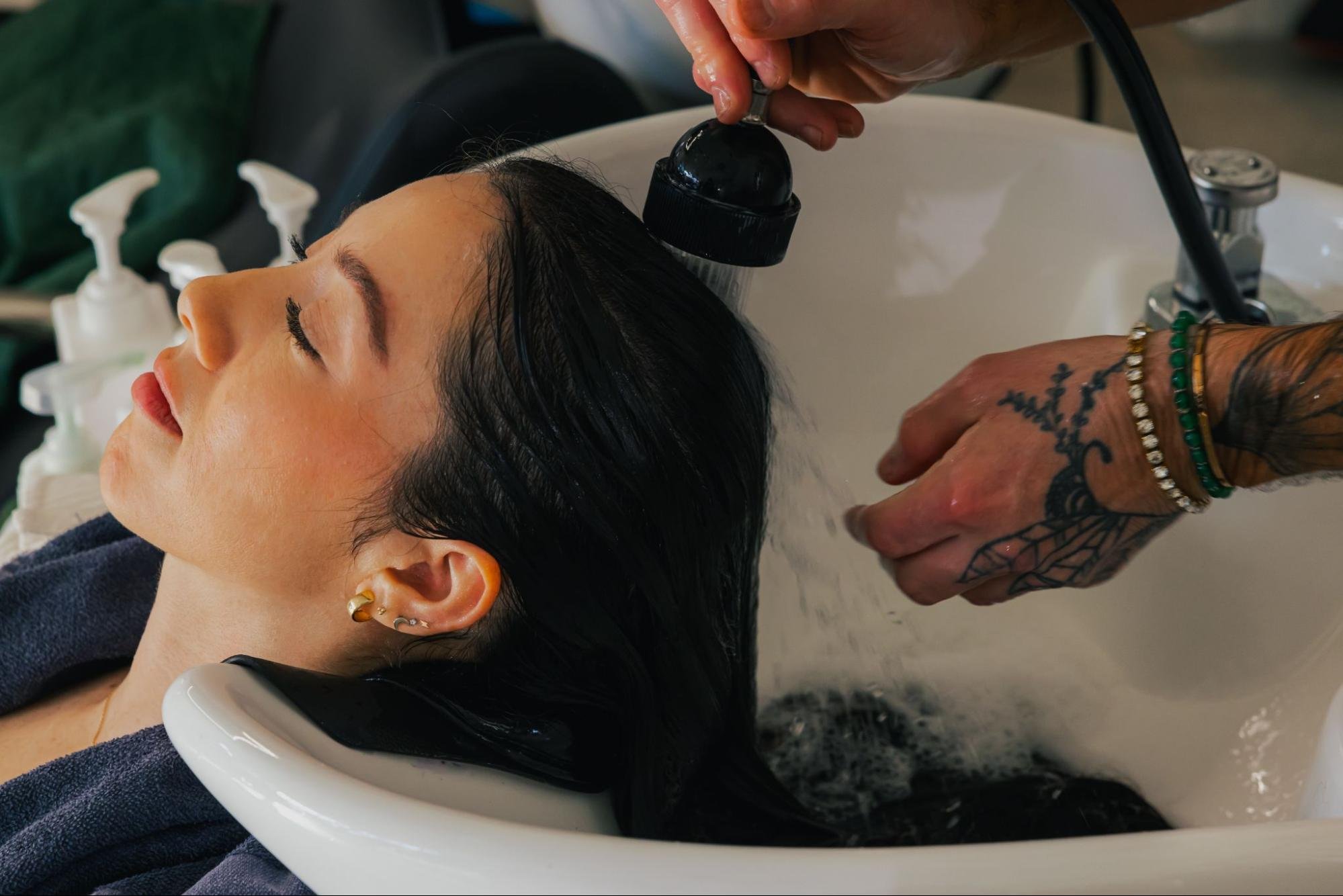 A salon client with long, dark hair leans back for a hair wash.