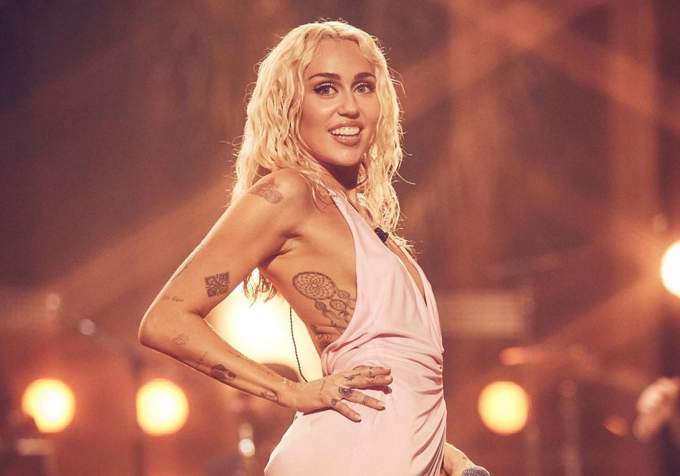 Miley Cyrus with platinum blonde wavy hair wearing a cream halter dress performing at the NYE party