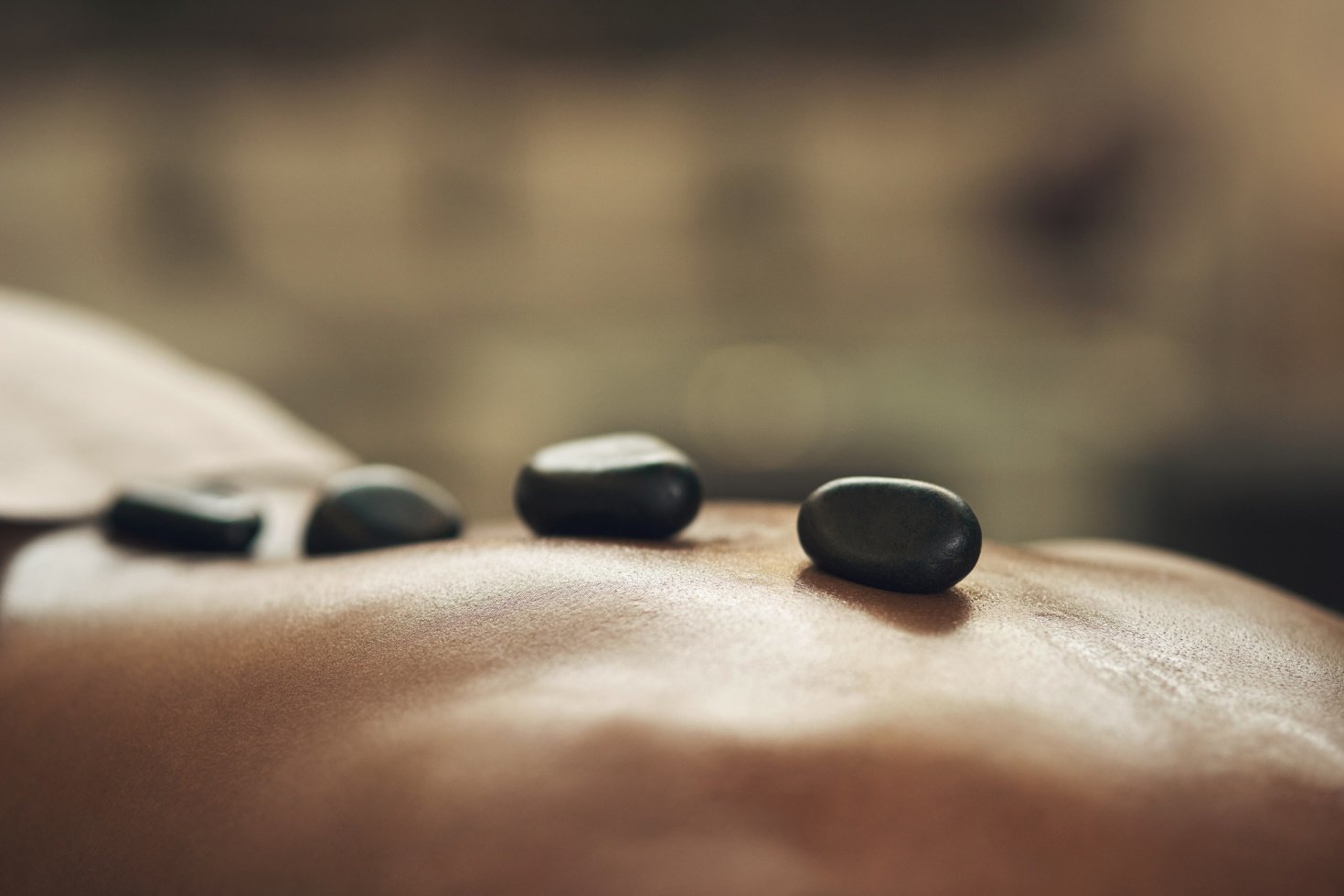 A row of shiny, tumbled black stones lay across a person's back.