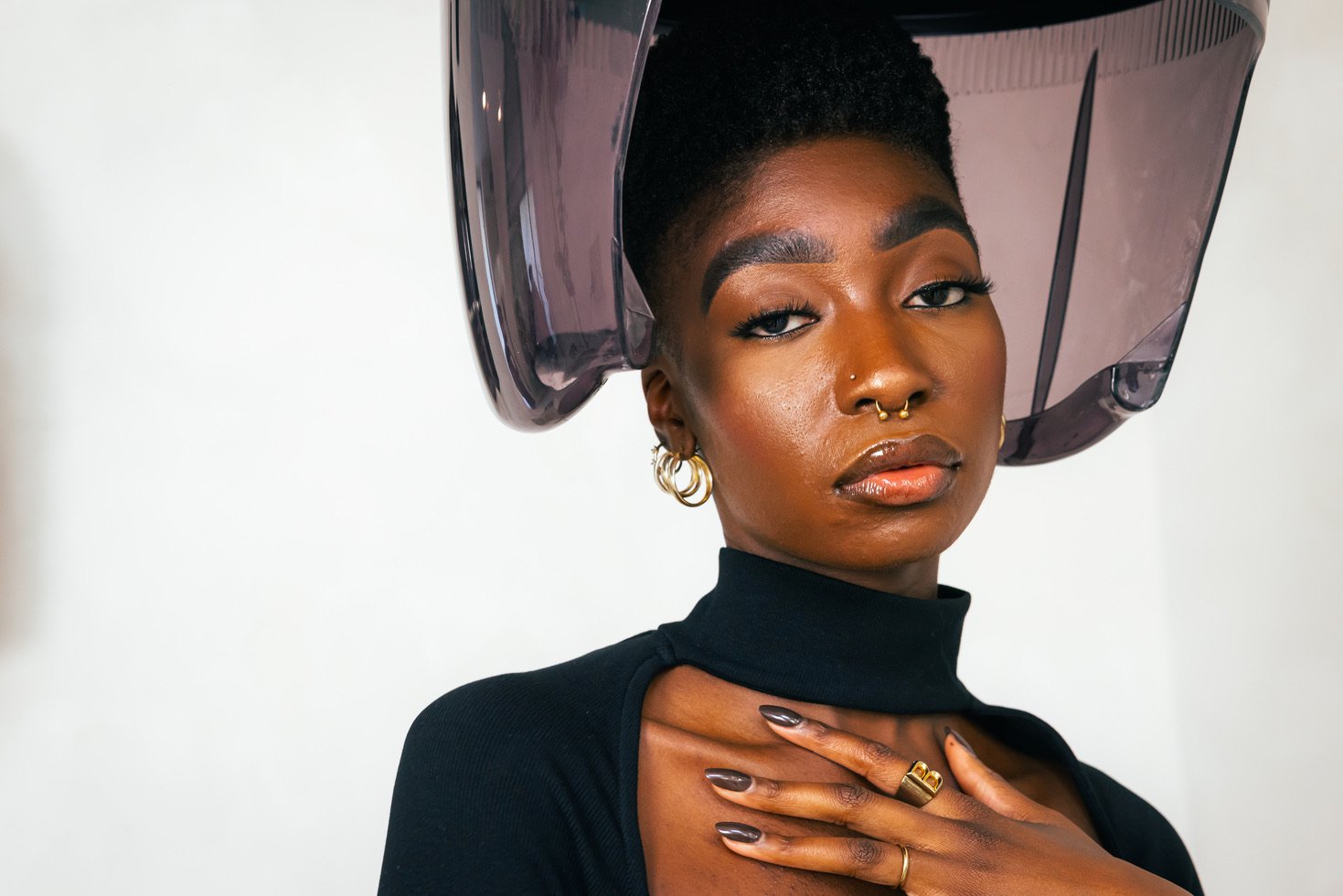 A woman with textured hair sits under a dryer at a hair salon.