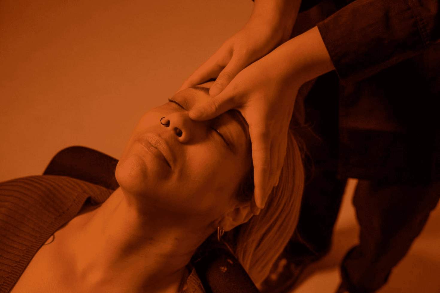 A relaxed-looking woman is leaning back in a chair with her eyes closed while a MedSpa pro touches her head.