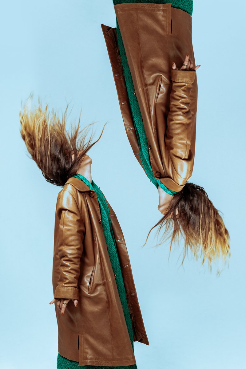 Mirrored, one side up, one upside down image of a woman in a trenchcoat and green sweater dress.