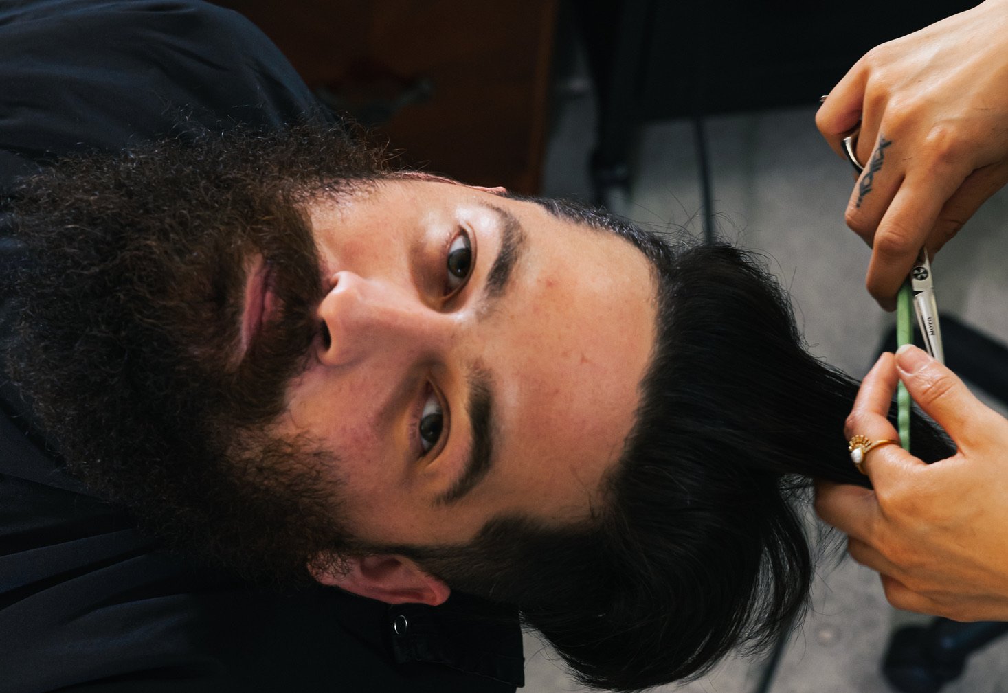 A client leans back in a chair and looks up at the camera while getting a haircut.