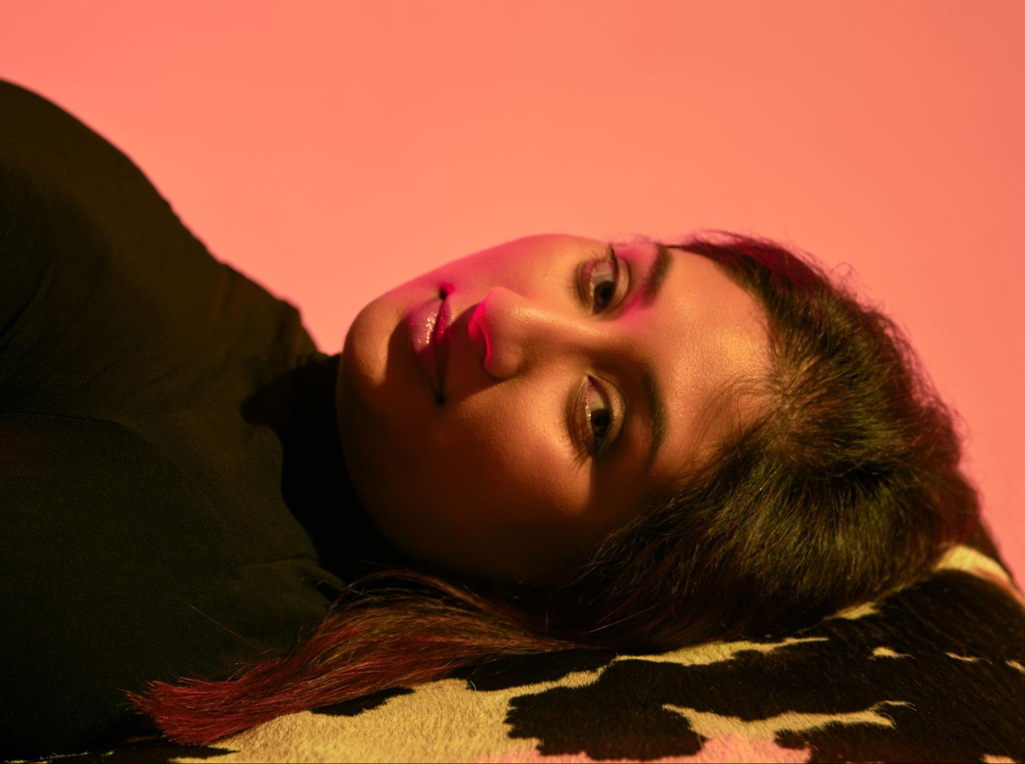 A person lays on their side and looks at the camera, illuminated by pink lighting.