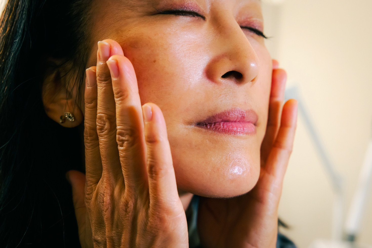 A closeup of a woman smoothing moisturizer into her cheeks.