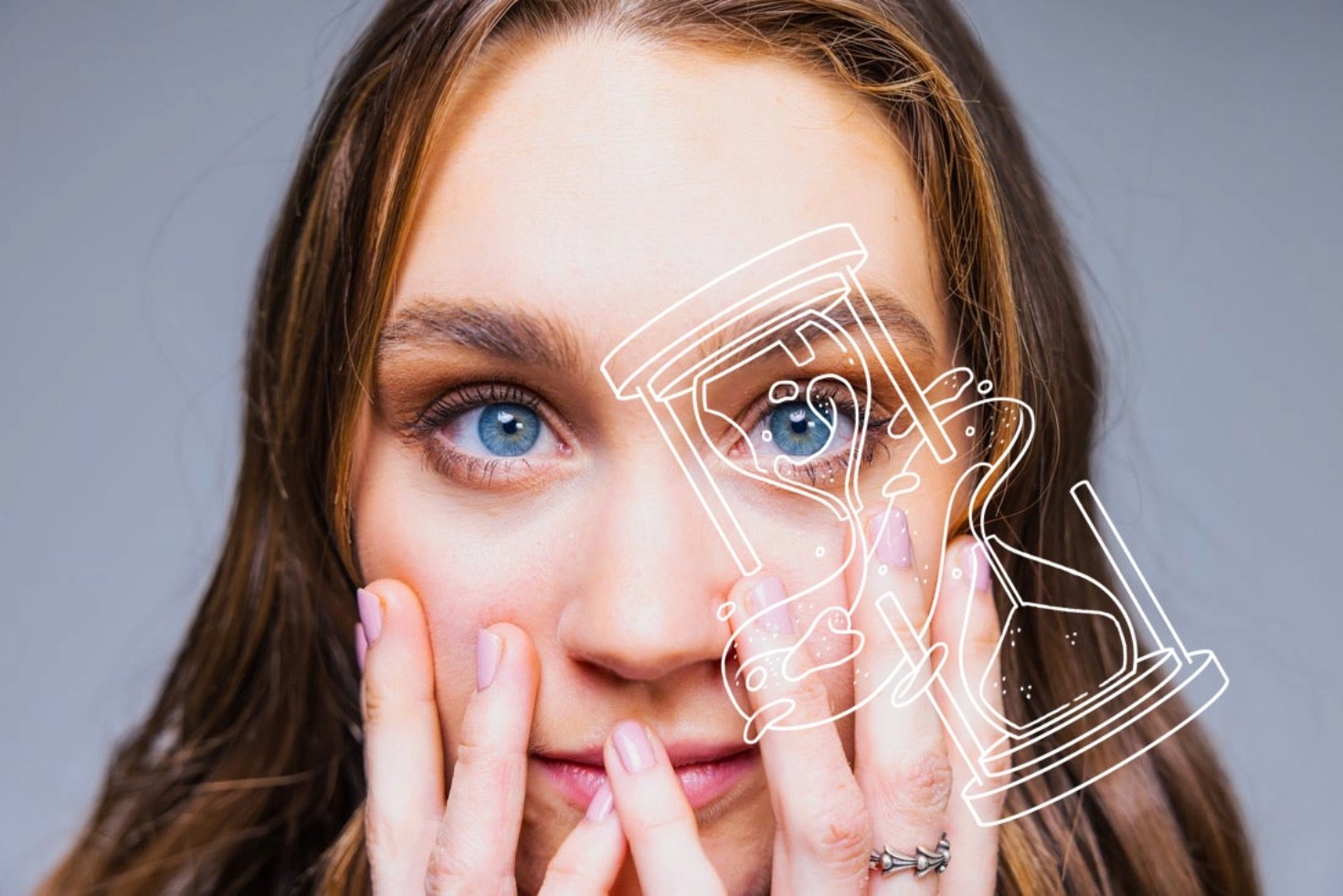 Photo illustration of a person with long brown hair and blue eyes looking at the camera with their fingers fanned out over their face. A white outline of a bisected hourglass is superimposed over their left eye.