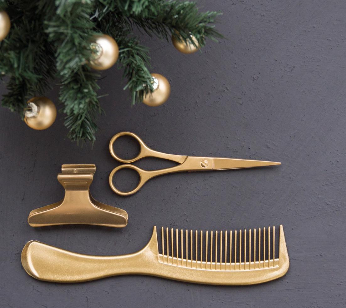 A gold comb, hair clip, and pair of scissors rest under the decorated branches of a fir tree.