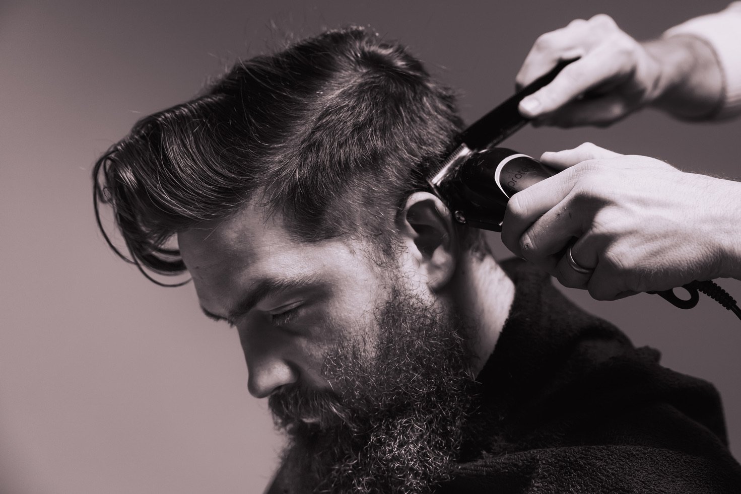 Black and white image of a barber shop patron receiving a trim around the ear.