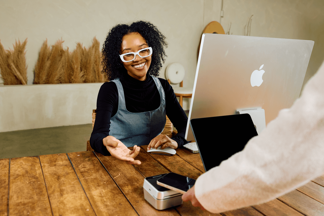 A self-care business clerk watches a client tap a smartphone on a payment terminal.
