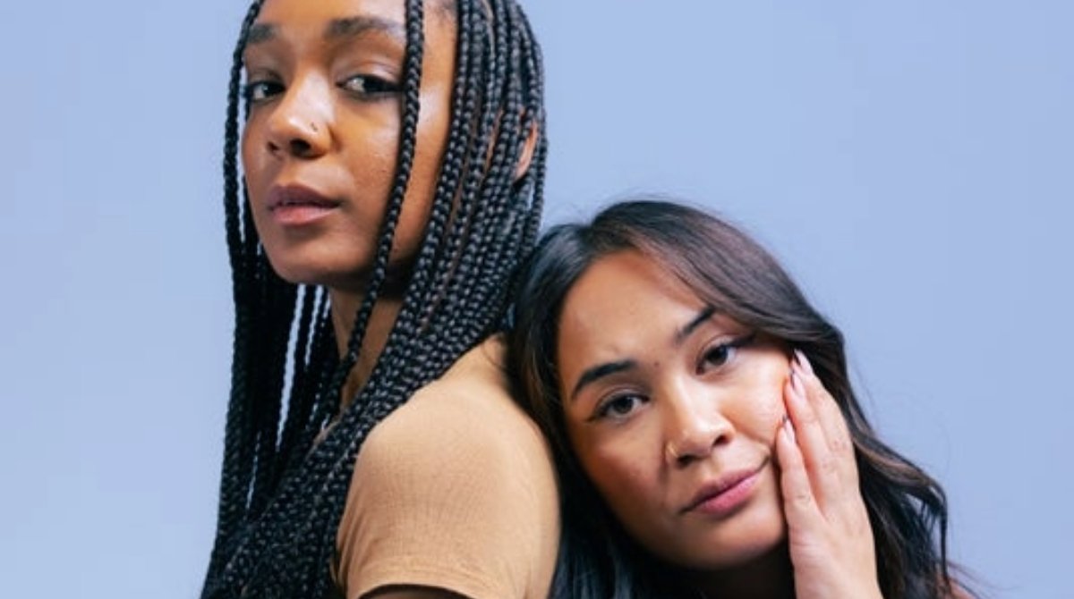 Two women lean on each other, back to back