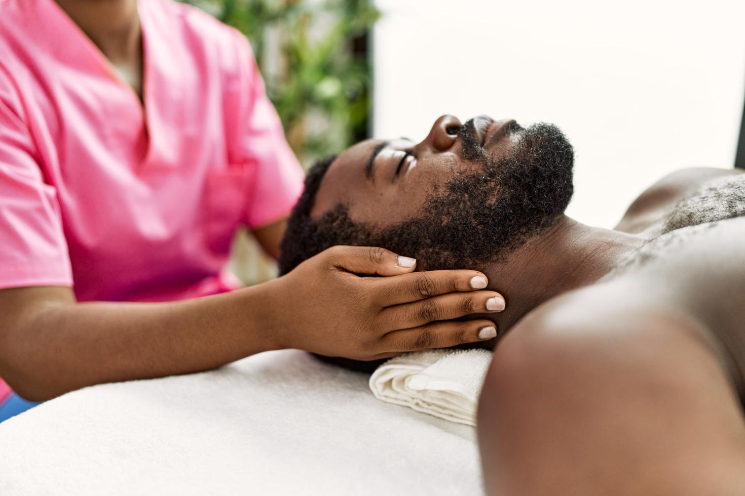 A man receives a head massage from a massage therapist wearing pink scrubs.