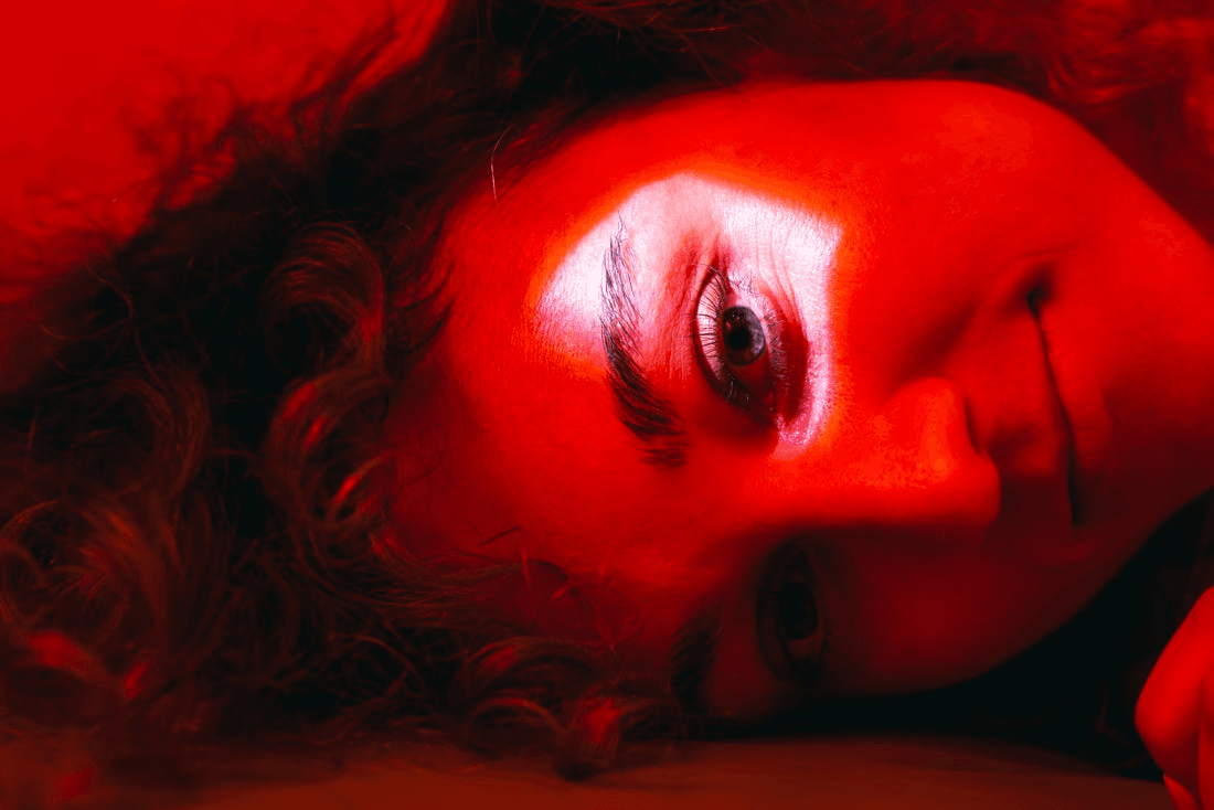 Close up of a woman's face in dim red light. There's a bright white spotlight on the eyebrow.