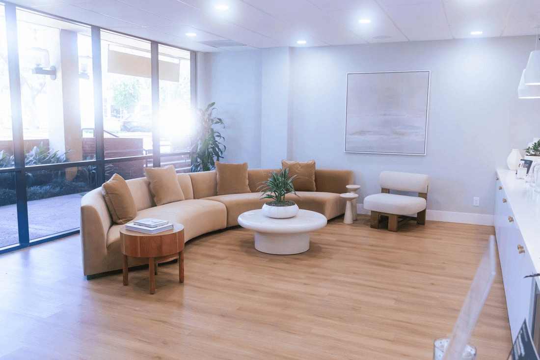Hardwood floors and a brown sectional couch adorn the waiting room of a medspa.
