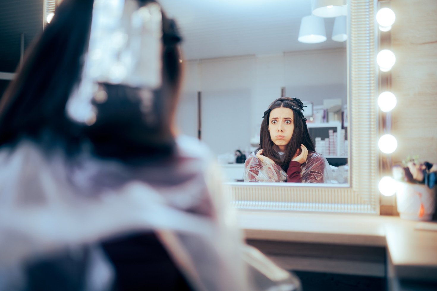 A woman seated in a salon chair makes a weird face into the mirror.