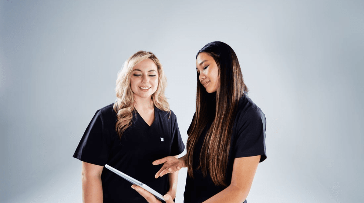 Two women wearing medical scrubs look at a digital tablet.