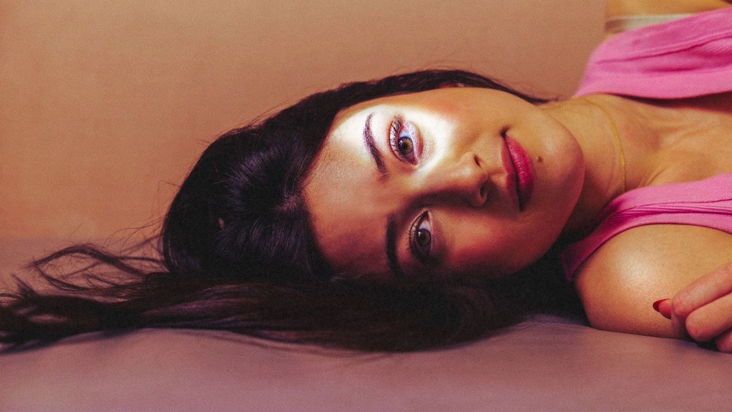 A woman laying on the fall of a pink to orange ombre backdrop.