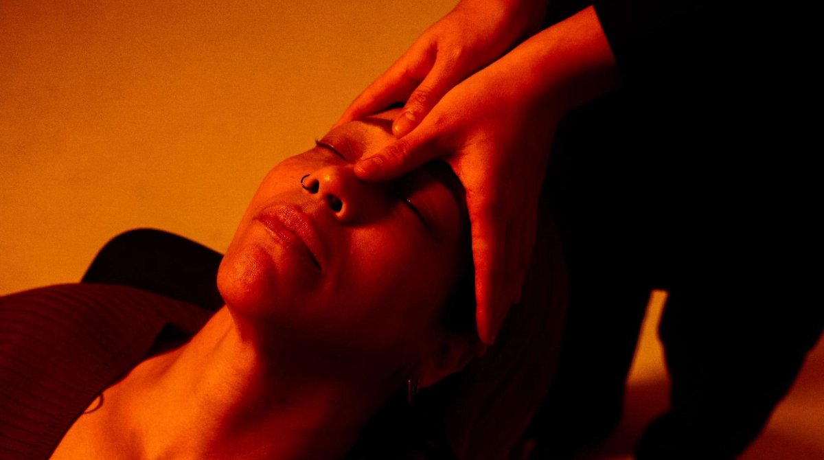 A woman illuminated by an orange light receives a face massage.