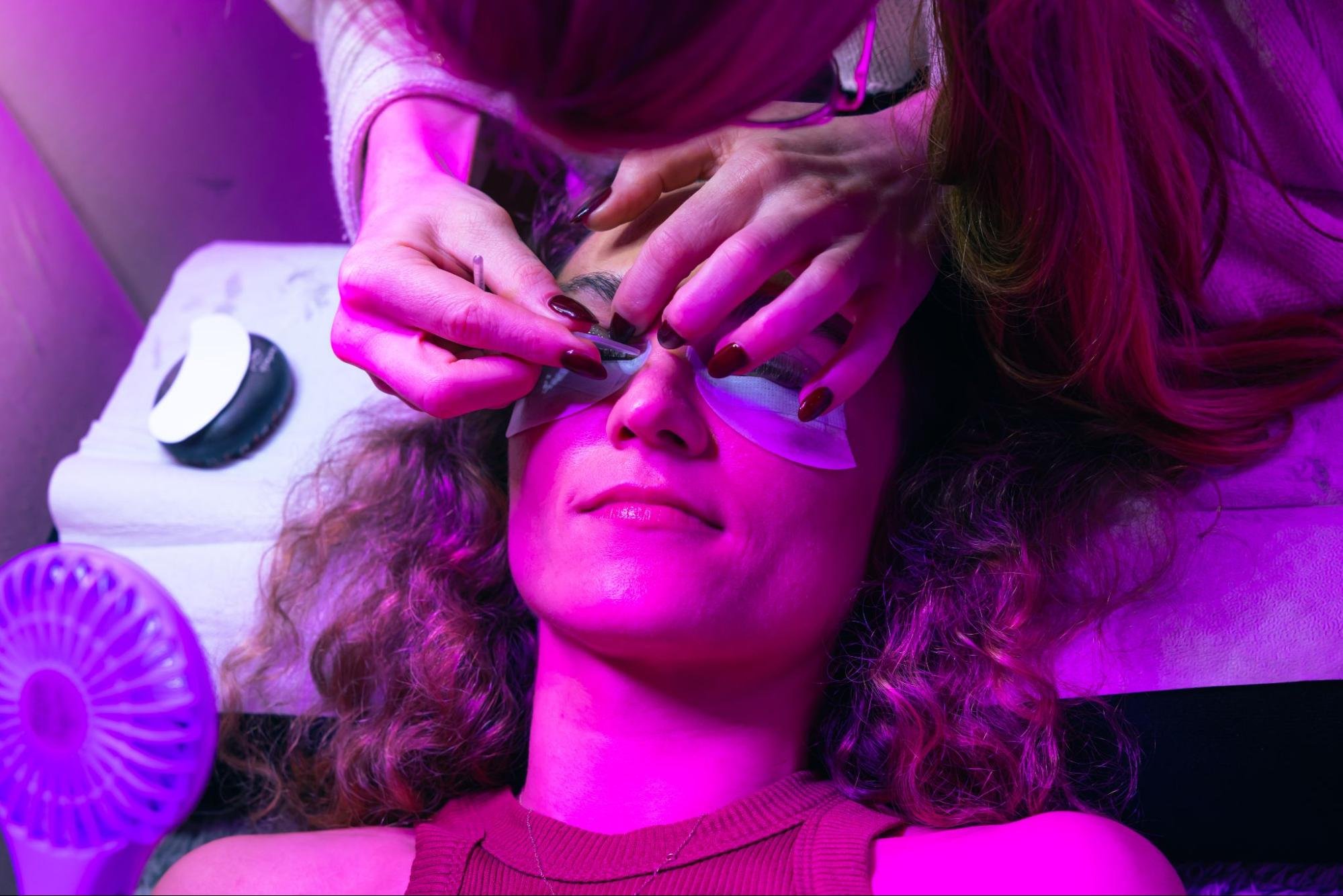 A client at Blink Bar gets their eyelashes worked on. A purple glow is emitting throughout the room.
