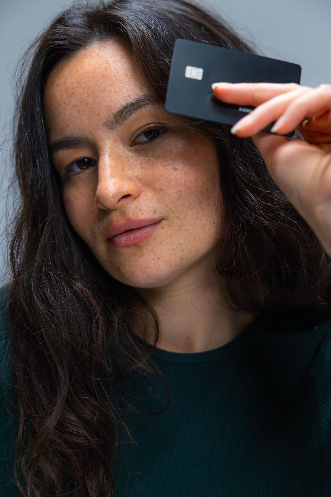 A freckled person holds their credit card close to the top of their head.