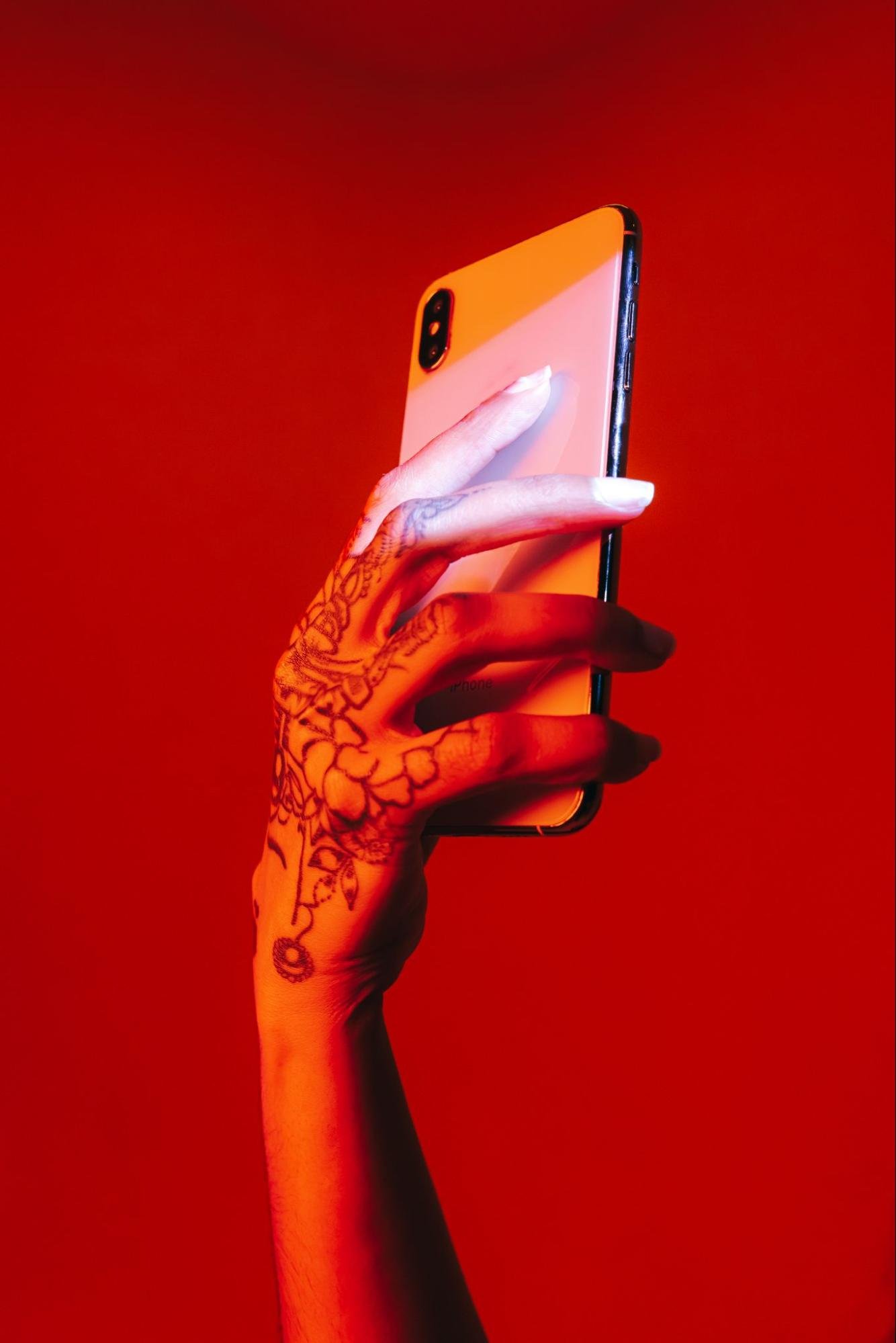 A beautiful hand clasps a smartphone against a red backdrop.